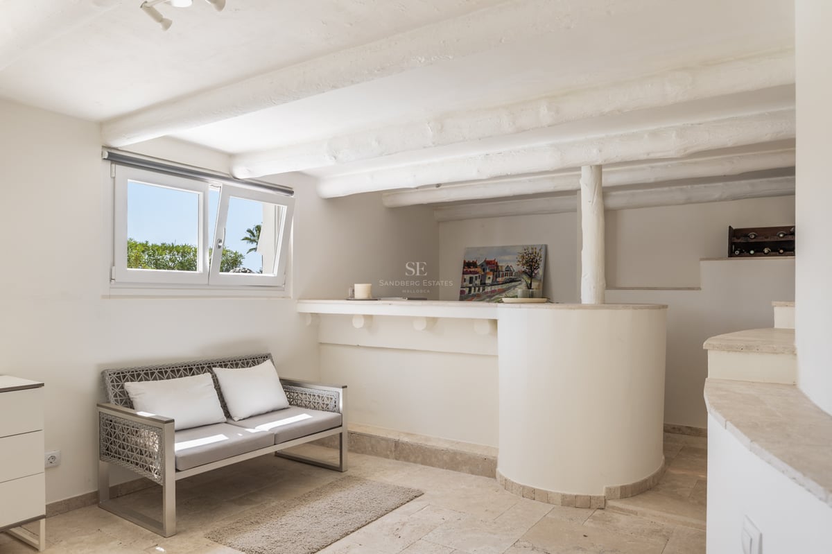 Intérieur blanc avec poutres en bois rustiques, sol en travertin, bar intégré et canapé moderne.