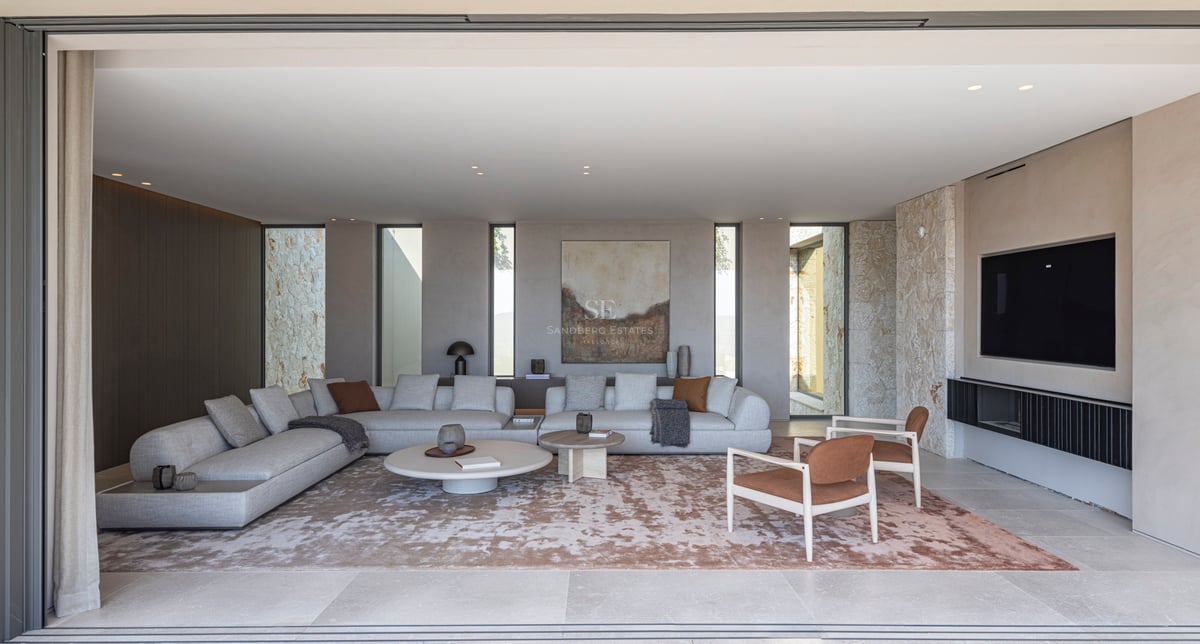 Un salon spacieux et moderne avec des canapés gris, un mur en pierre naturelle et de grandes baies vitrées.