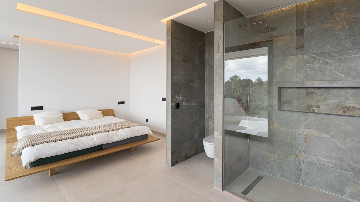 Chambre moderne avec lit flottant en bois et salle de bain ouverte avec carrelage en pierre grise et douche vitrée.