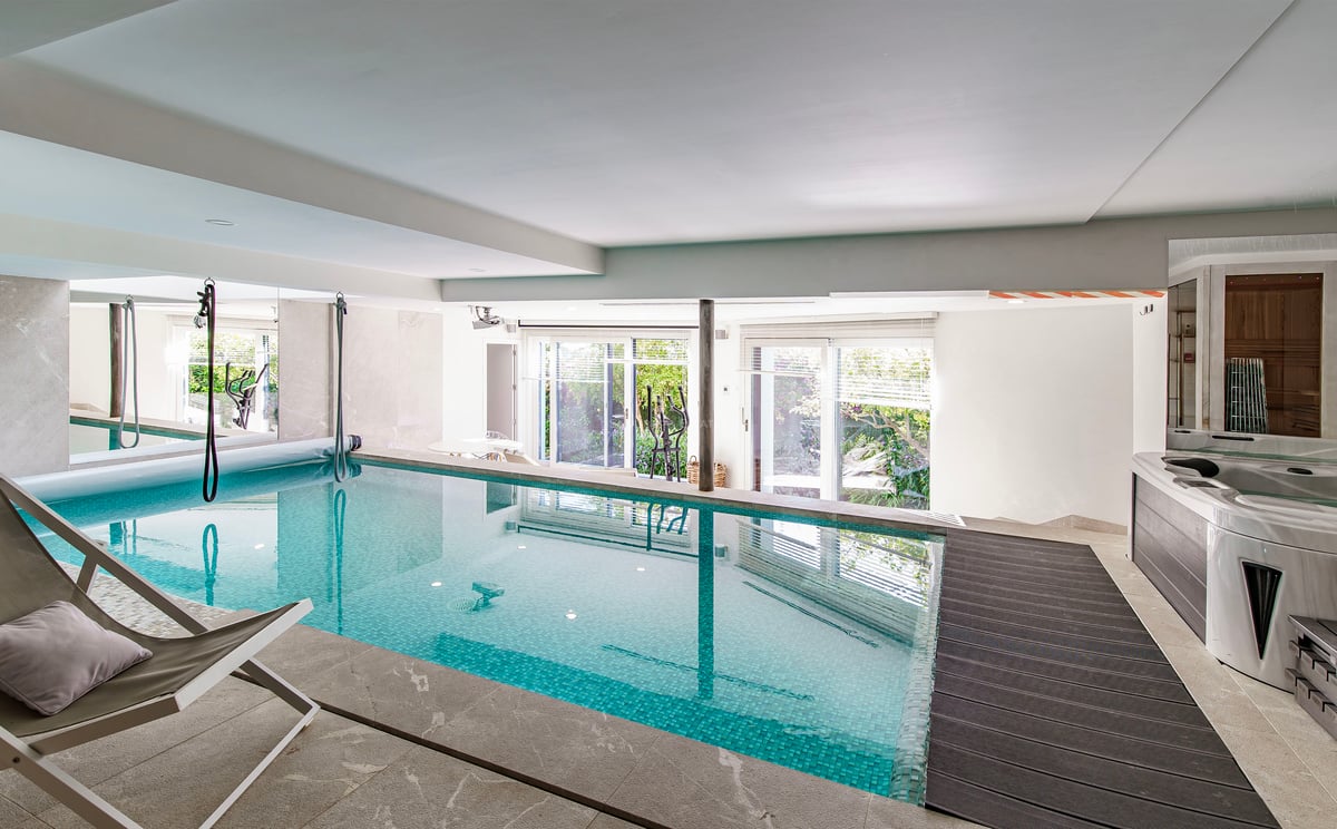 Piscine intérieure en mosaïque turquoise, jacuzzi et accès direct au jardin par des baies vitrées.