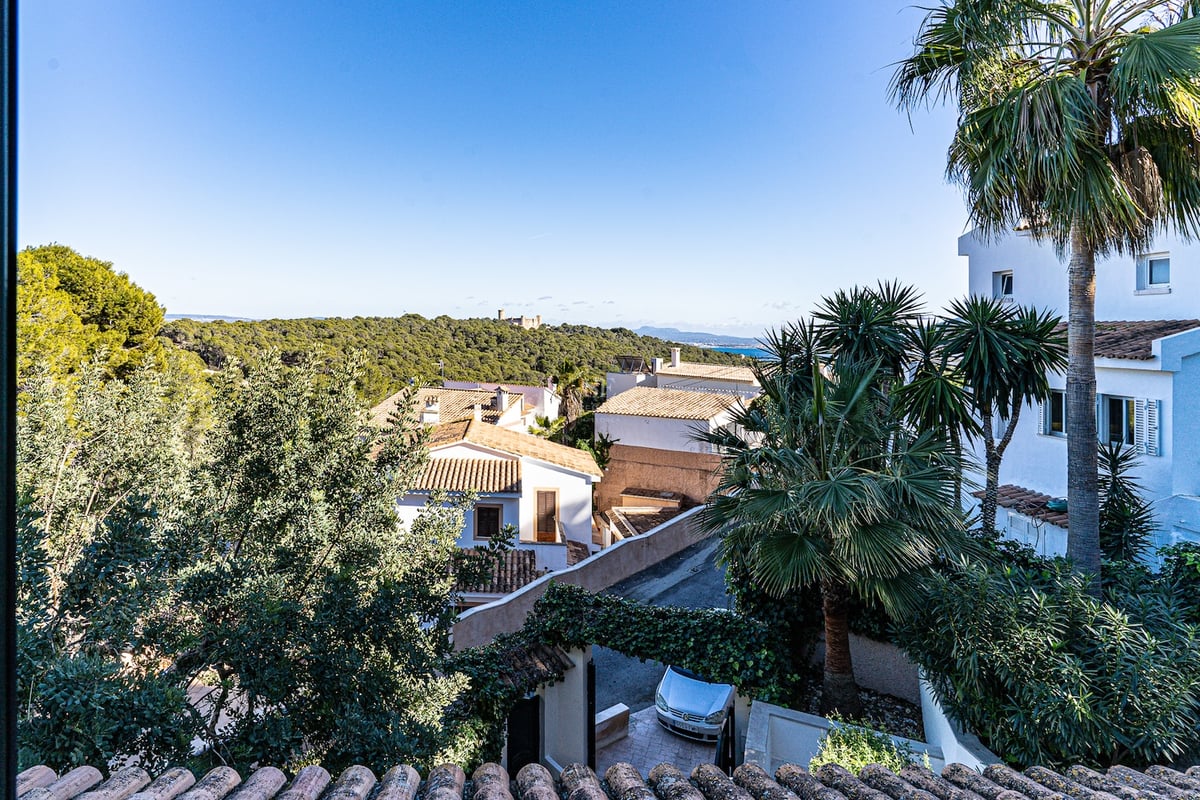 Vue panoramique en hauteur montrant des villas blanches, une végétation luxuriante, un château au loin et la mer.