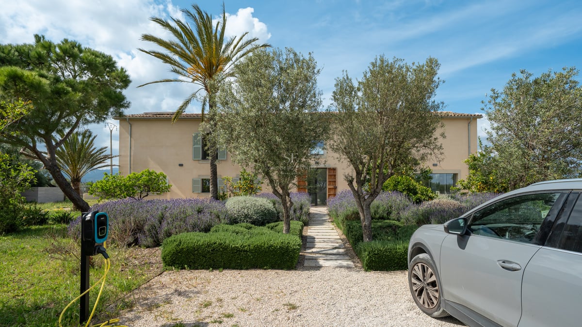 Façade d'une villa ocre avec jardin de lavande, sentier en pierre et borne pour véhicule électrique.