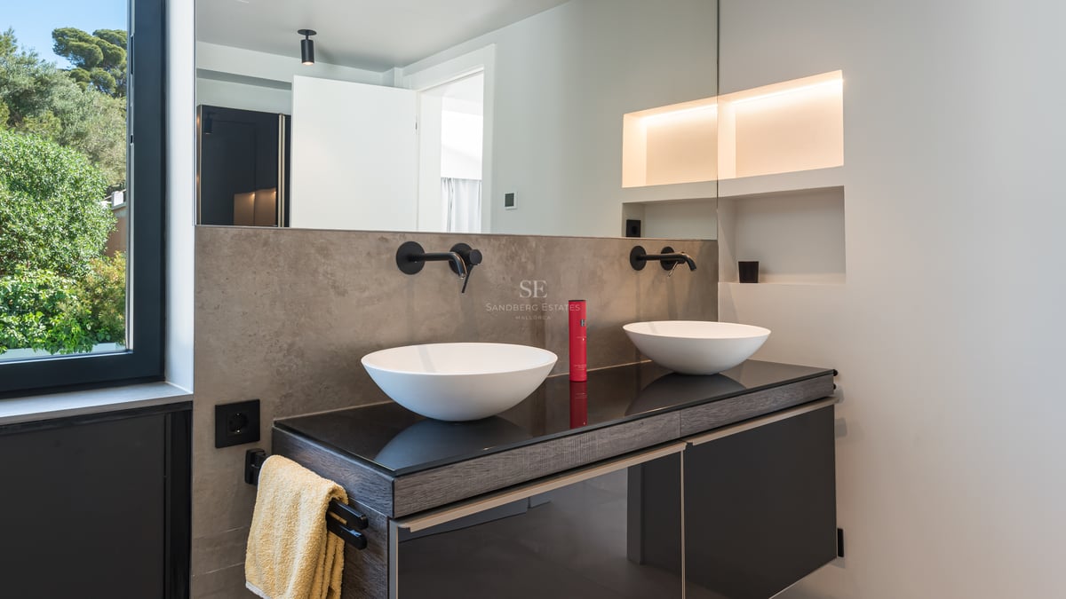Salle de bains contemporaine avec deux vasques blanches, robinetterie murale noire mate et éclairage d'ambiance.