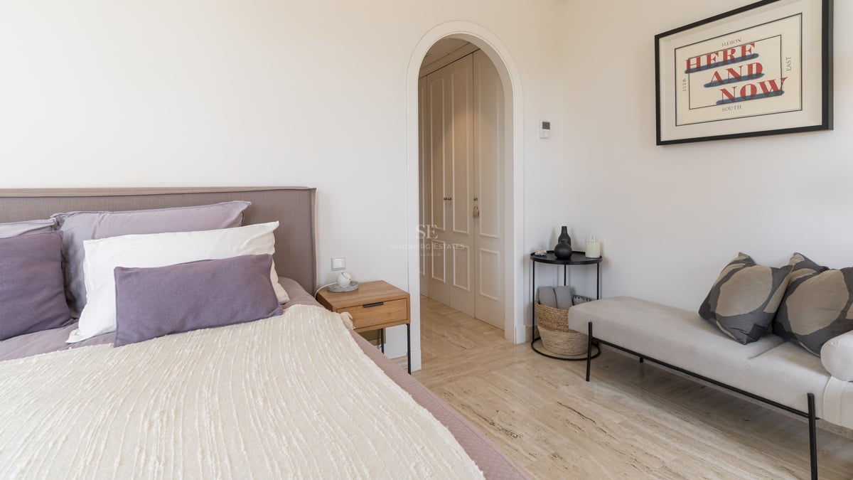 Chambre moderne avec lit rembourré mauve, sol en marbre travertin et arche menant au dressing.