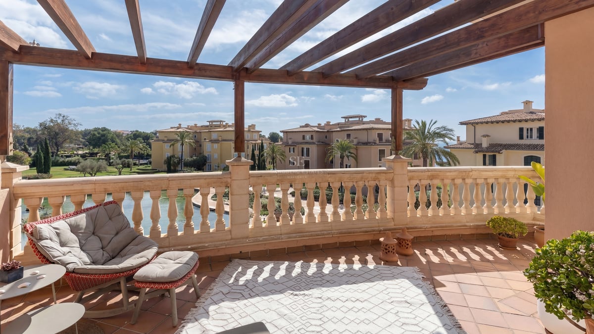 Terrasse ensoleillée avec pergola en bois, balustrade en pierre et tapis extérieur donnant sur des palmiers.