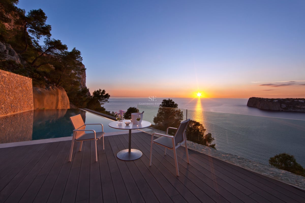 Coucher de soleil depuis une terrasse de luxe avec piscine à débordement et mobilier moderne blanc.