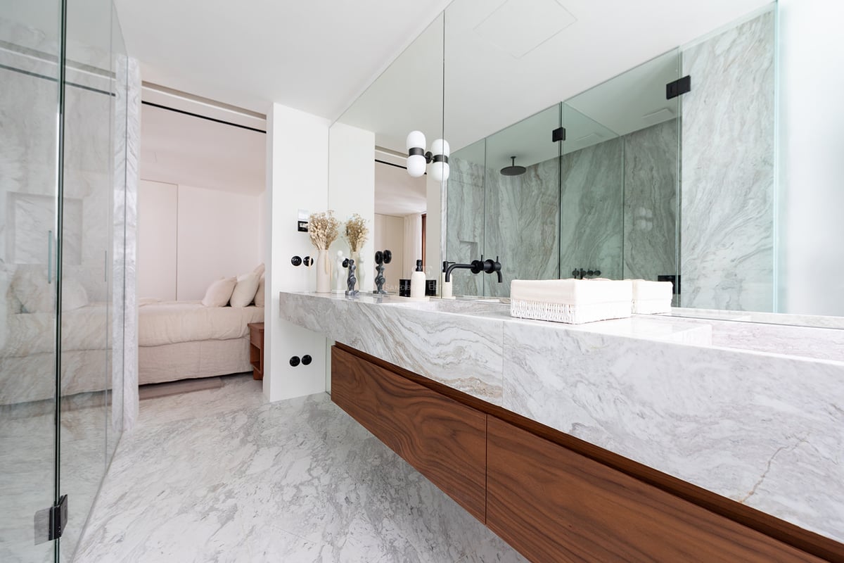 Baño moderno con lavabo doble de mármol, muebles de nogal y ducha de vidrio integrada.