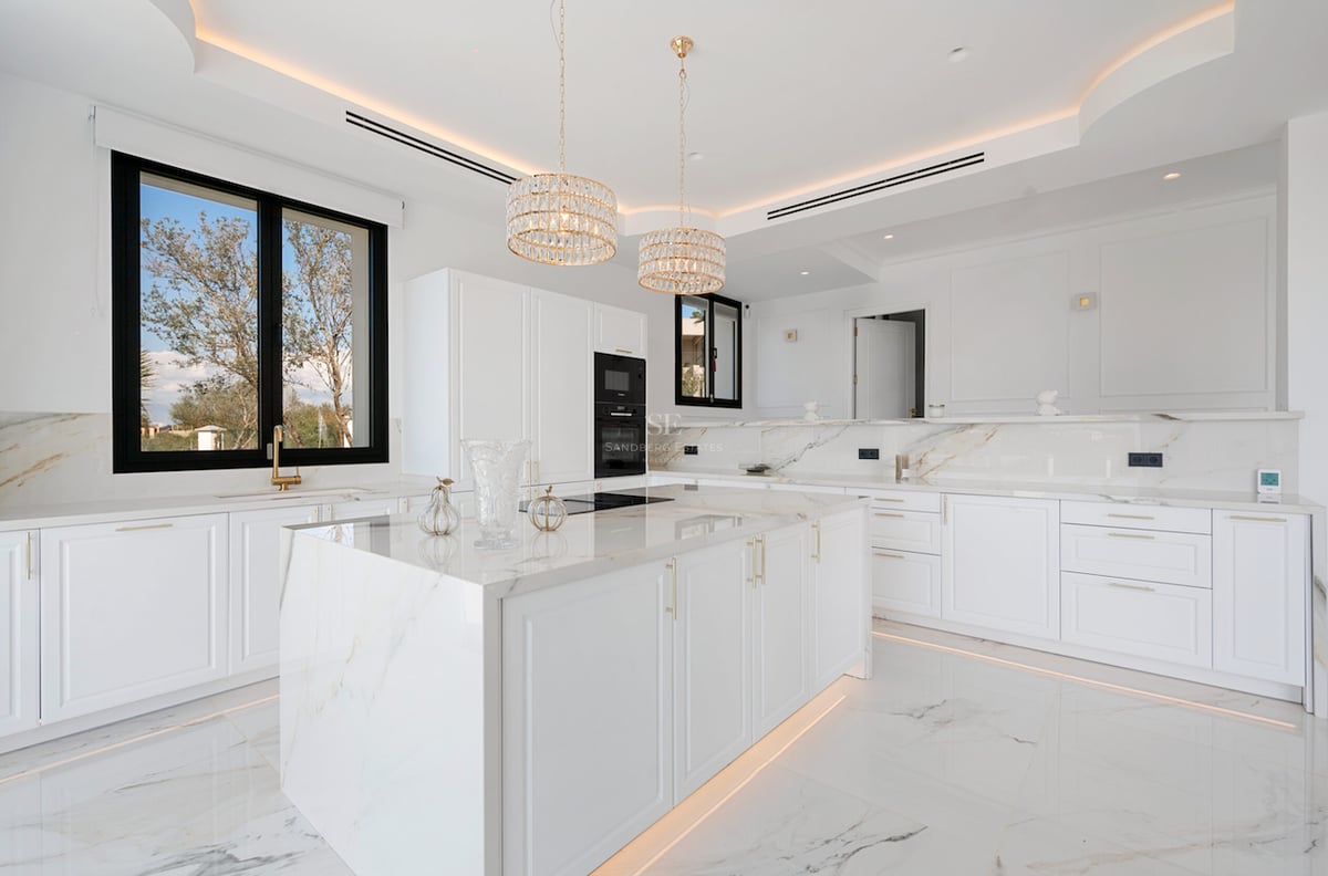 Cuisine moderne lumineuse avec îlot en marbre blanc, finitions dorées et grandes fenêtres.