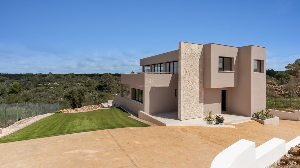 Villa moderne de deux étages avec façade sable, accents en pierre naturelle et grandes baies vitrées sur la pelouse.