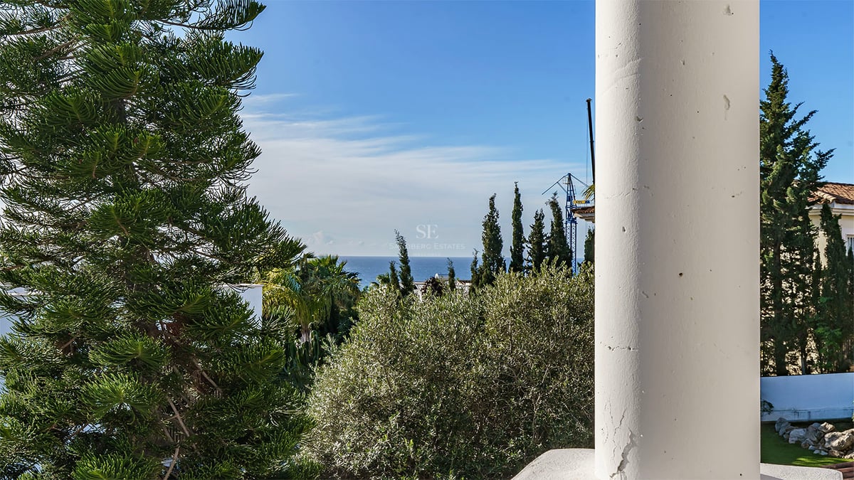 Vue sur la mer Méditerranée encadrée par une colonne blanche et une végétation luxuriante sous un ciel bleu.