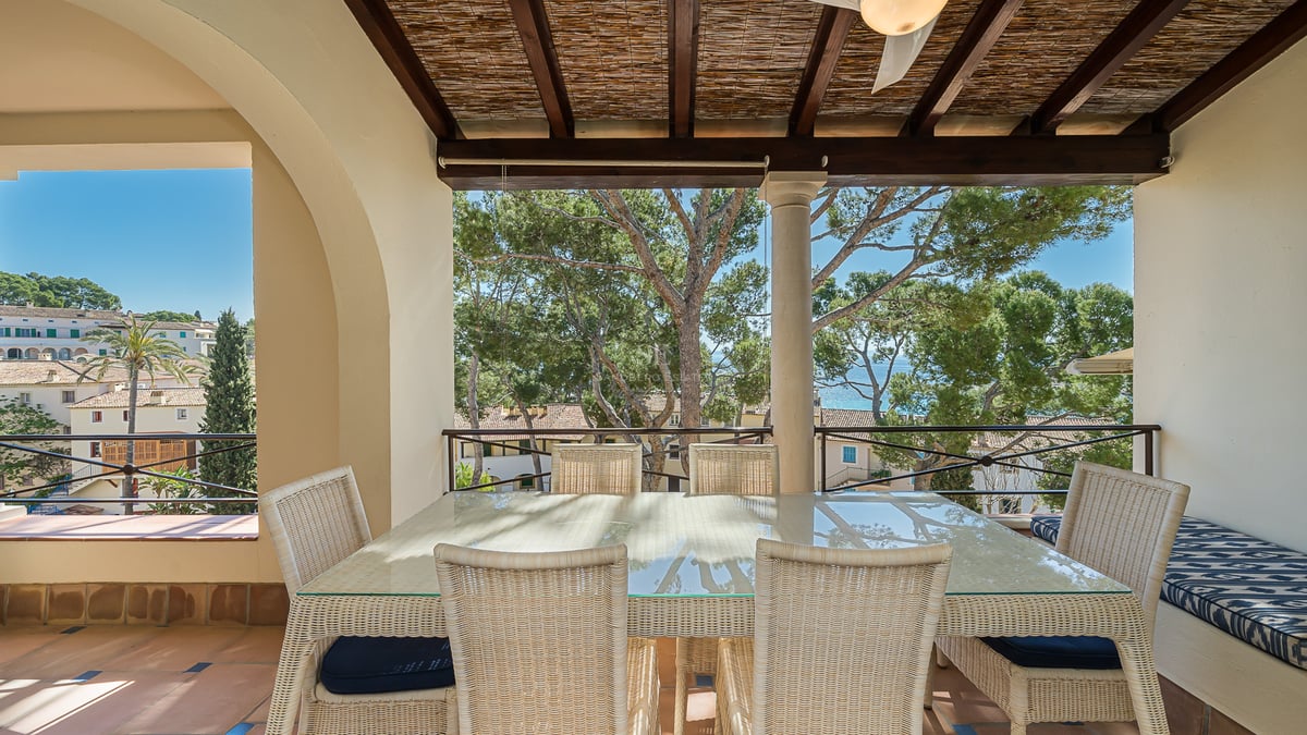 Terrasse couverte avec salle à manger en osier, sol en terre cuite et vue sur les pins et la mer.