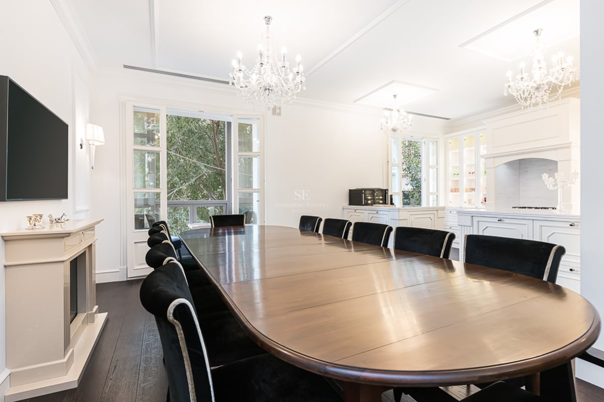 Grande table à manger en bois et chaises en velours noir sous des lustres en cristal dans une pièce blanche lumineuse.