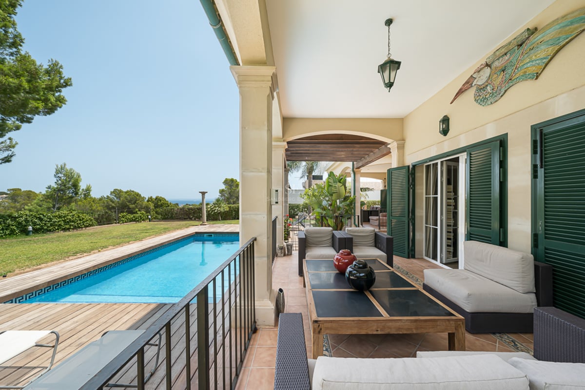 Porche couvert avec salon de jardin donnant sur une piscine, une terrasse en bois et la mer au loin.