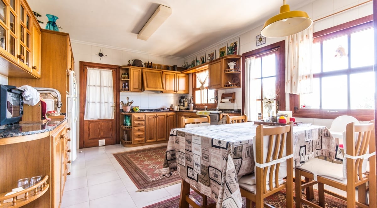 Cuisine rustique lumineuse avec des armoires en bois, une table à manger avec nappe et de la lumière naturelle.