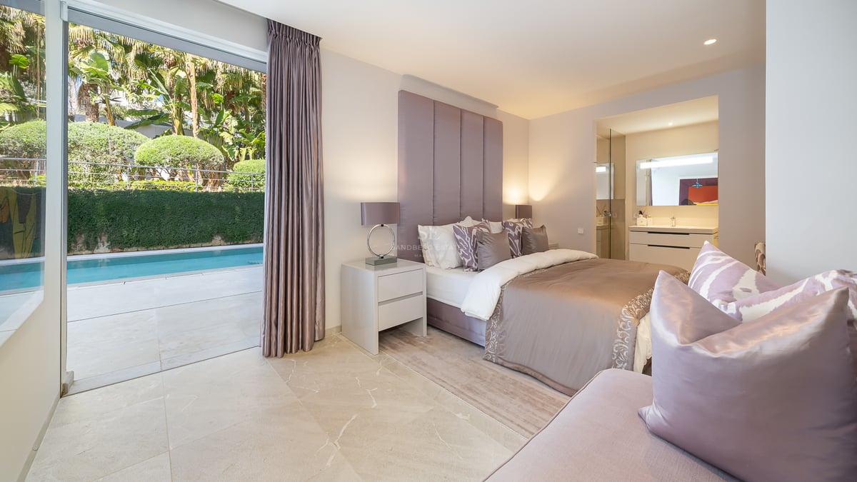 Chambre moderne avec lit double, tête de lit capitonnée, sol en marbre et accès direct à une piscine extérieure.