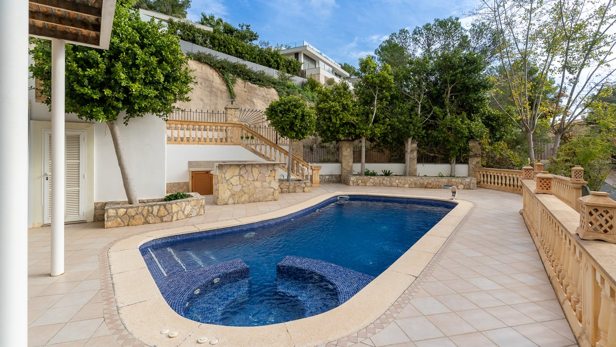 Piscine bleue avec sièges intégrés sur une terrasse carrelée entourée de balustrades et d'arbres.