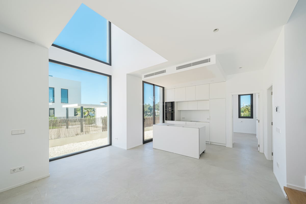 Cuisine blanche minimaliste avec îlot, baies vitrées double hauteur et lumière naturelle abondante.