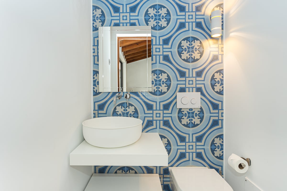 Salle d'eau avec carrelage bleu à motifs, vasque blanche sur étagère flottante et miroir rectangulaire.