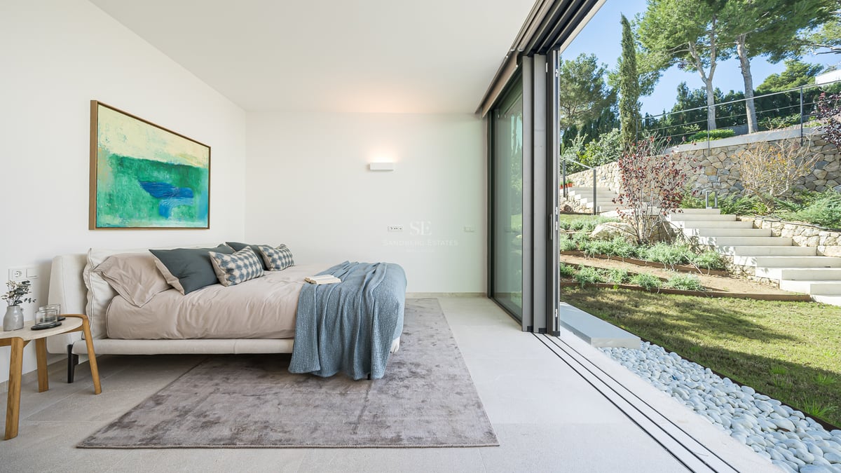 Chambre moderne avec baies vitrées donnant sur un jardin paysager avec escaliers en pierre et pelouse.