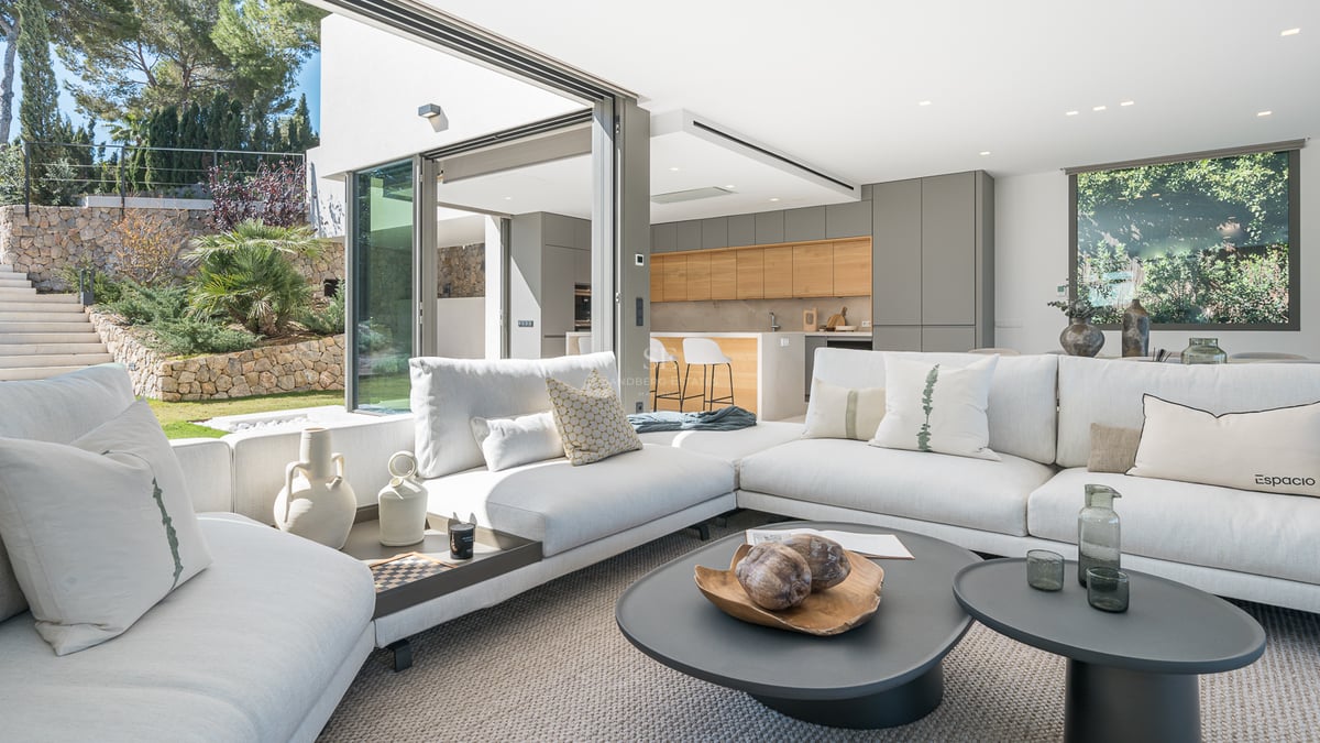 Grand salon blanc avec canapés modernes, baies vitrées sur le jardin et cuisine intégrée.