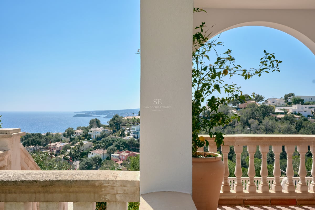 Terrasse méditerranéenne avec arches blanches et balustrade en pierre surplombant la côte et la mer bleue.