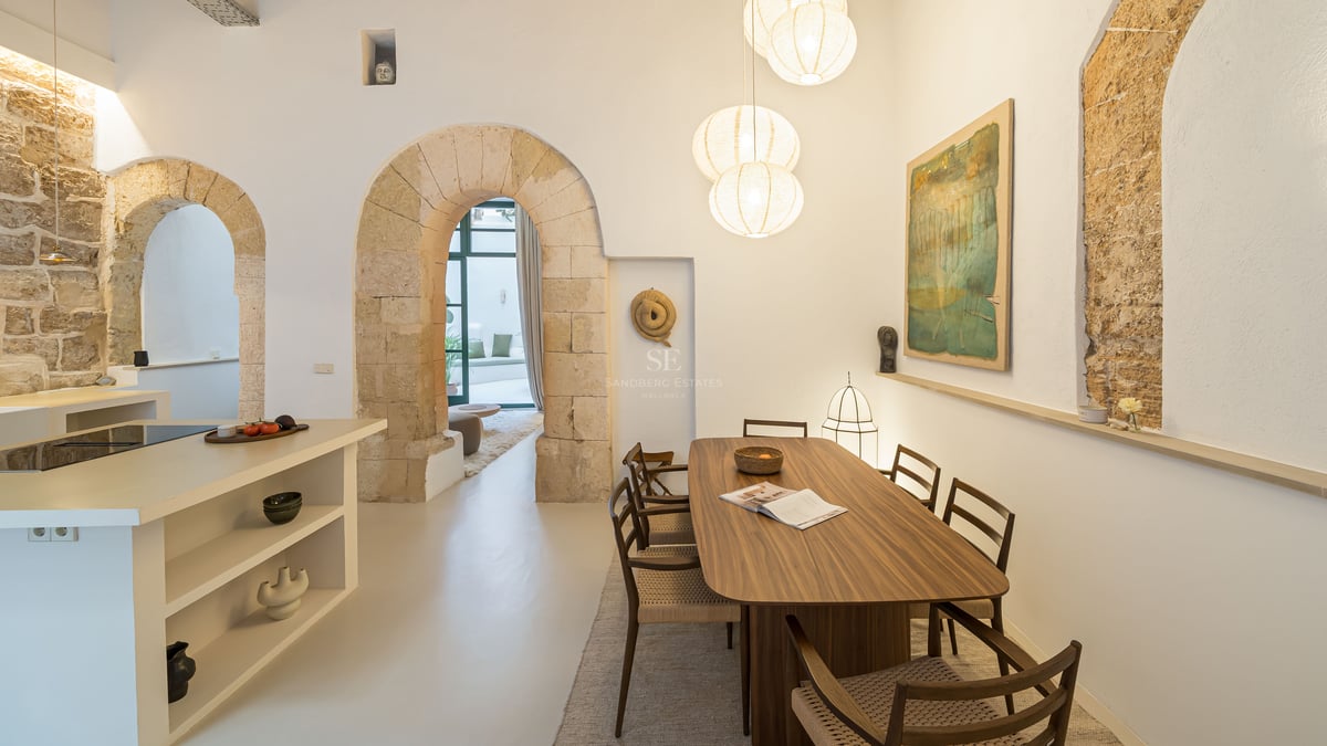 Salle à manger contemporaine avec table en bois sous des suspensions globes, encadrée par des arches en pierre.