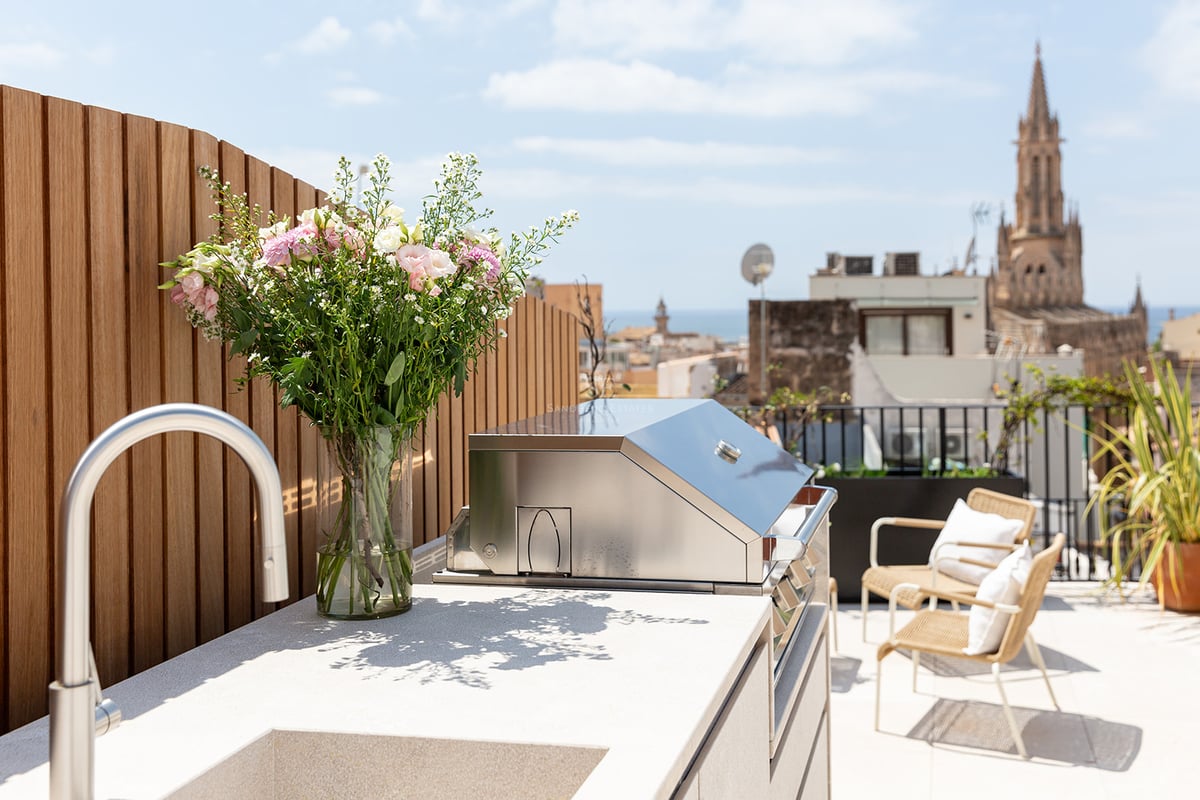 Terraza moderna con barbacoa de acero inoxidable, encimera de piedra y vistas a la catedral bajo un cielo despejado.