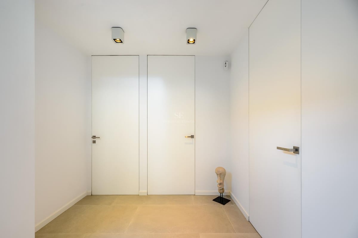 Couloir minimaliste avec portes blanches affleurantes, sol en pierre claire et petite sculpture décorative.