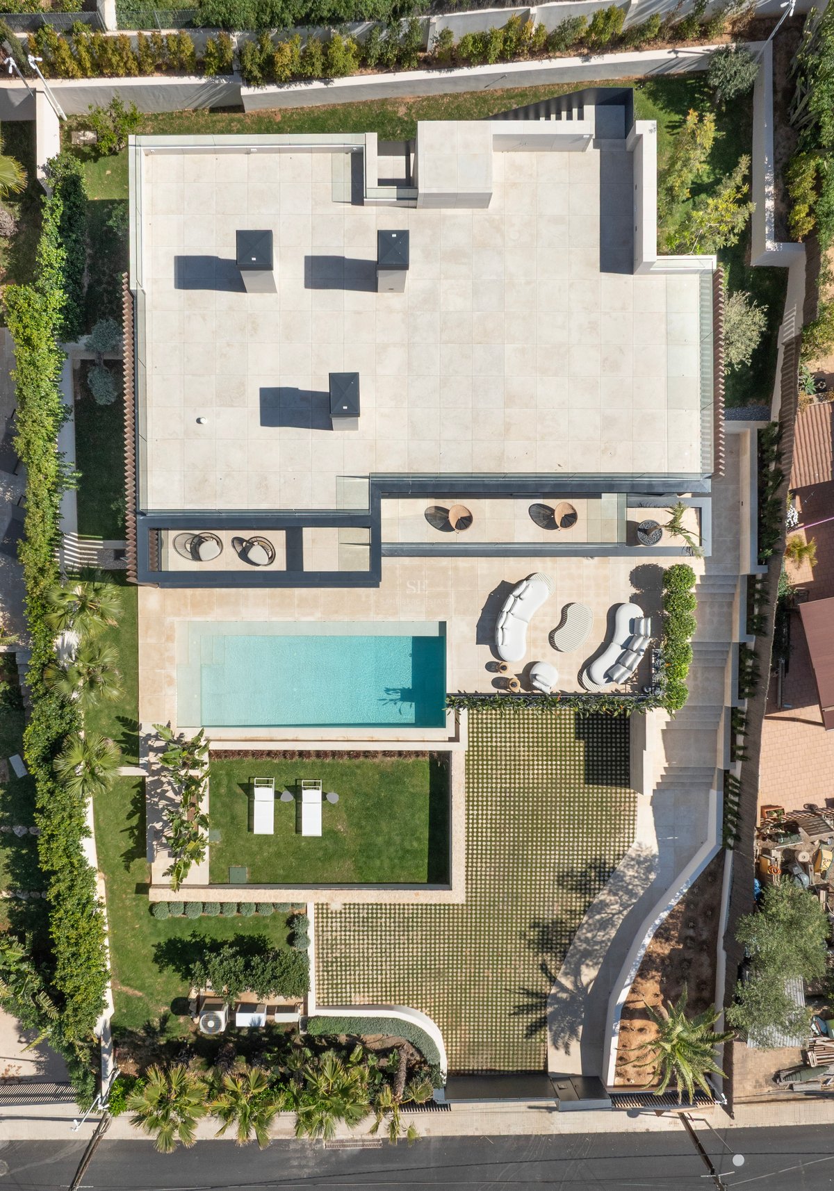 Vue plongeante d'une villa moderne avec piscine, transats, salon extérieur et jardins paysagers.