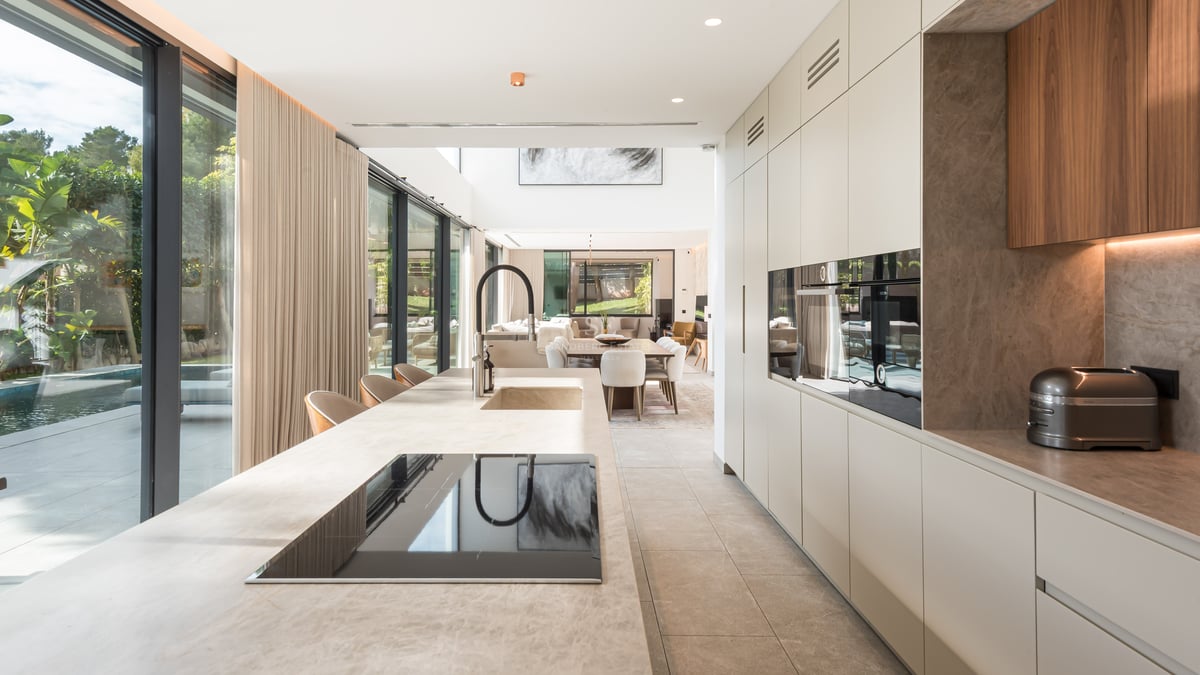 Cuisine moderne avec un grand îlot en pierre, des appareils intégrés et des baies vitrées donnant sur une piscine.