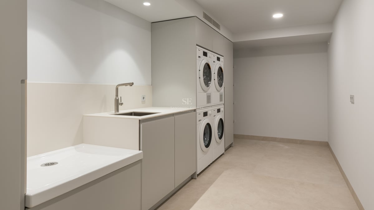 Buanderie moderne équipée de lave-linge et sèche-linge Miele, rangements épurés et grand bac de lavage.