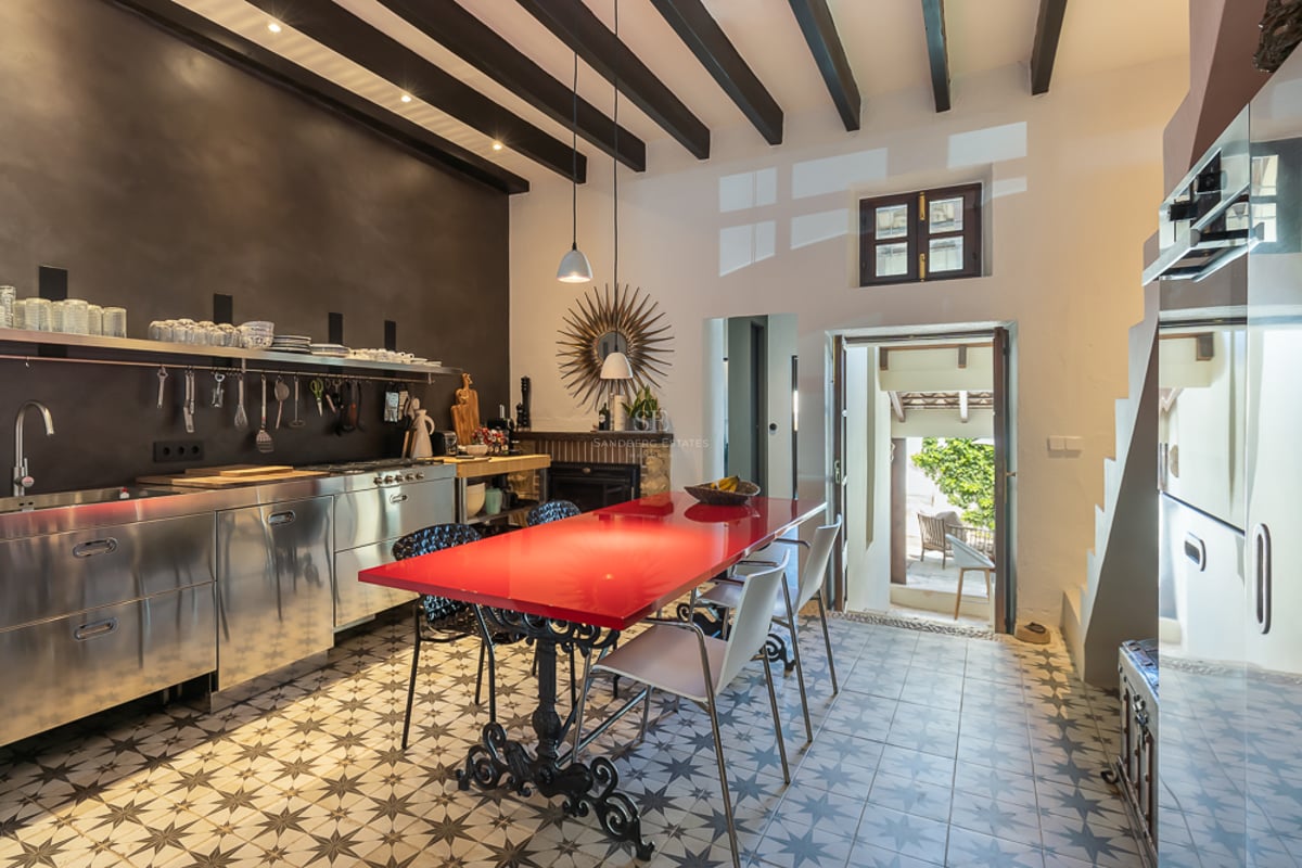 Modern kitchen featuring stainless steel cabinets, a red dining table, and traditional patterned floor tiles.
