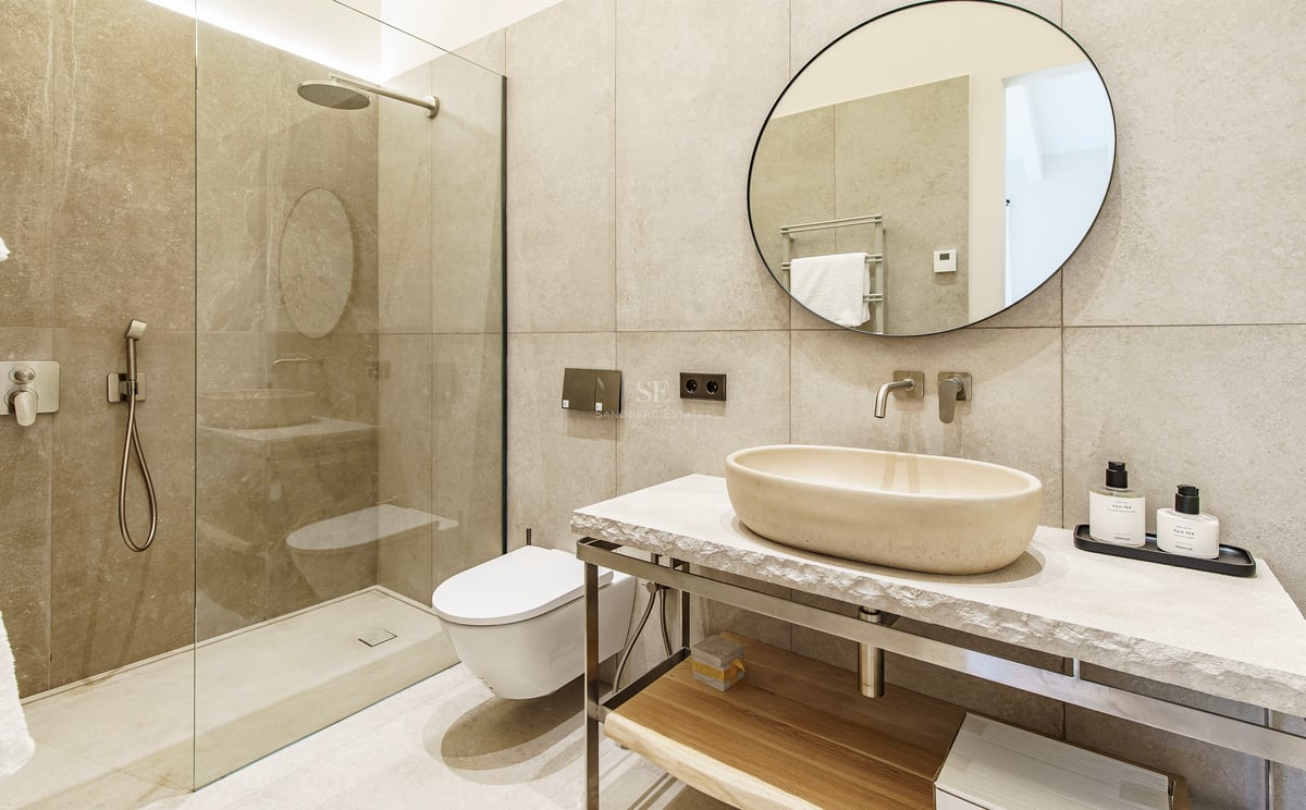 Baño contemporáneo con lavabo de piedra sobre encimera, espejo redondo y ducha de obra con mampara de cristal.