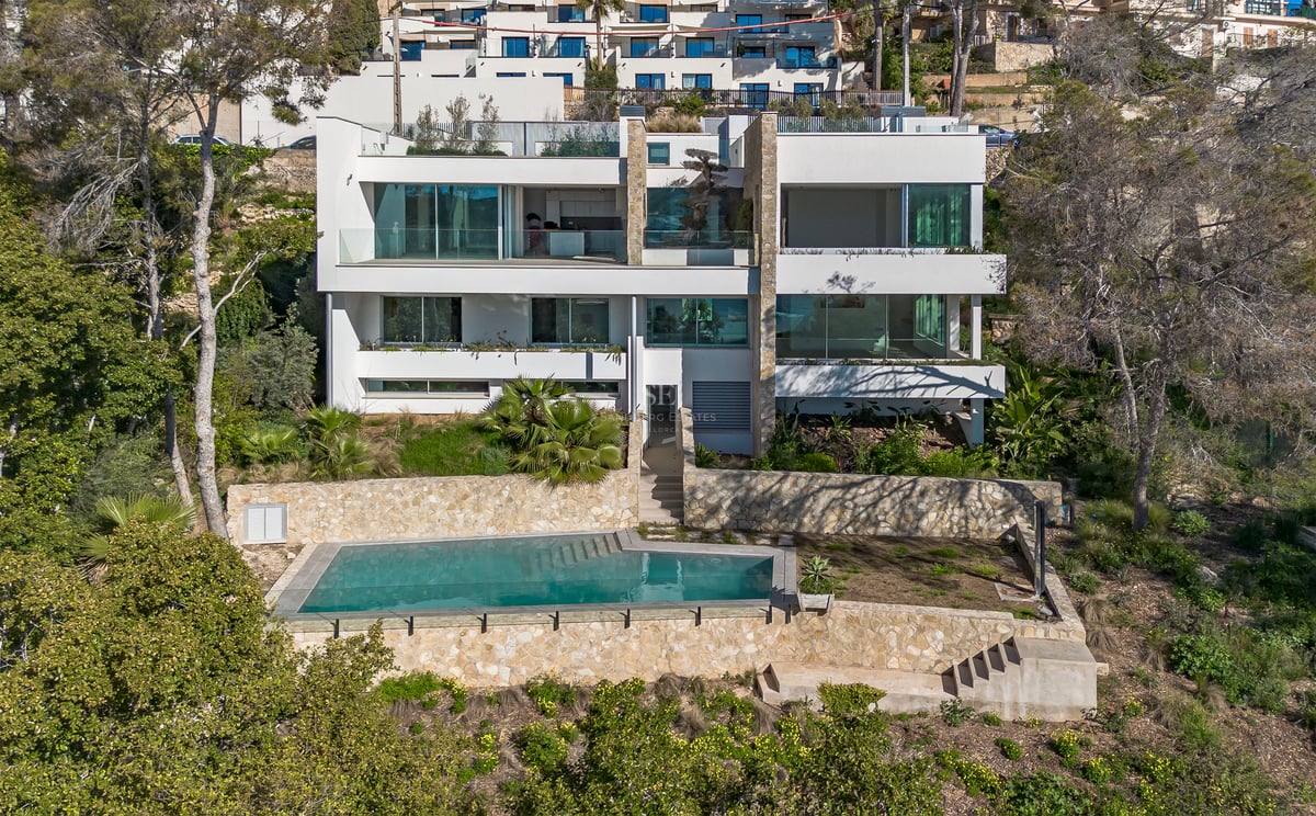 Vue extérieure d'une villa blanche à trois niveaux avec baies vitrées et piscine encadrée de murs en pierre.