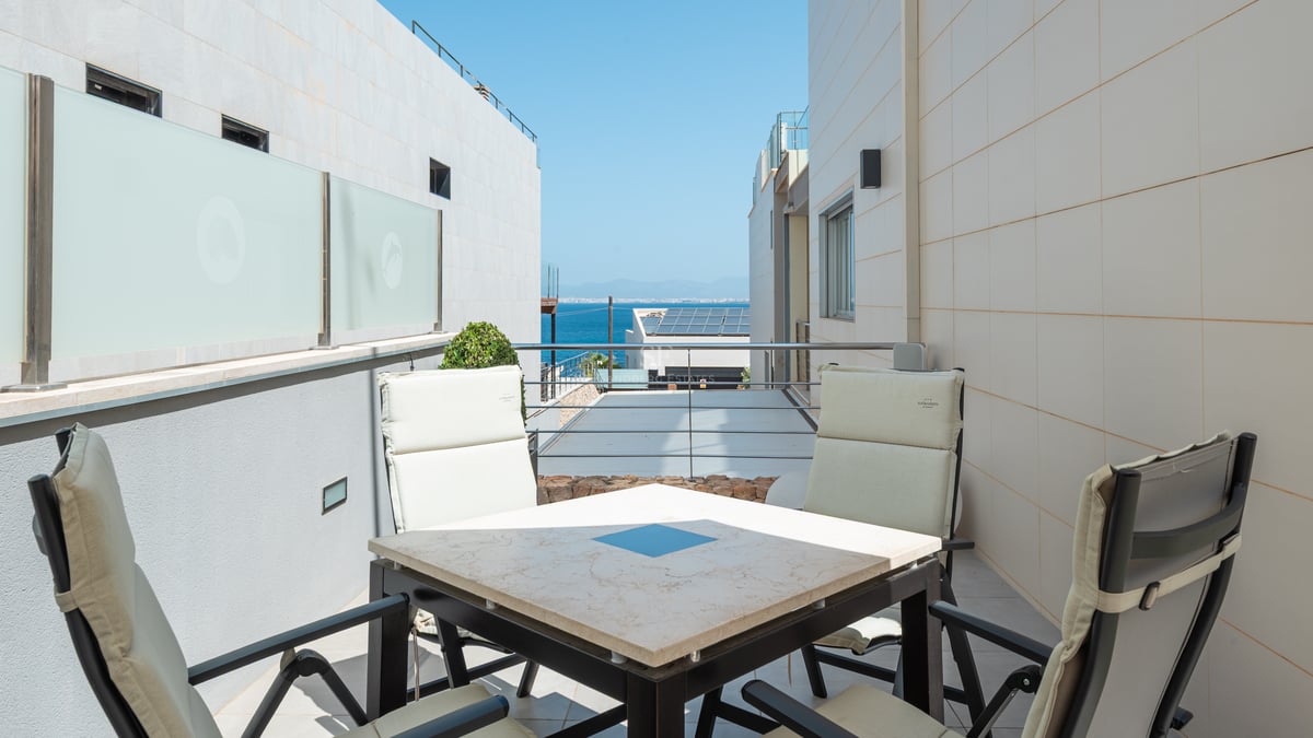 Terrasse privée avec table en pierre et chaises offrant une vue sur la mer entre des bâtiments blancs.