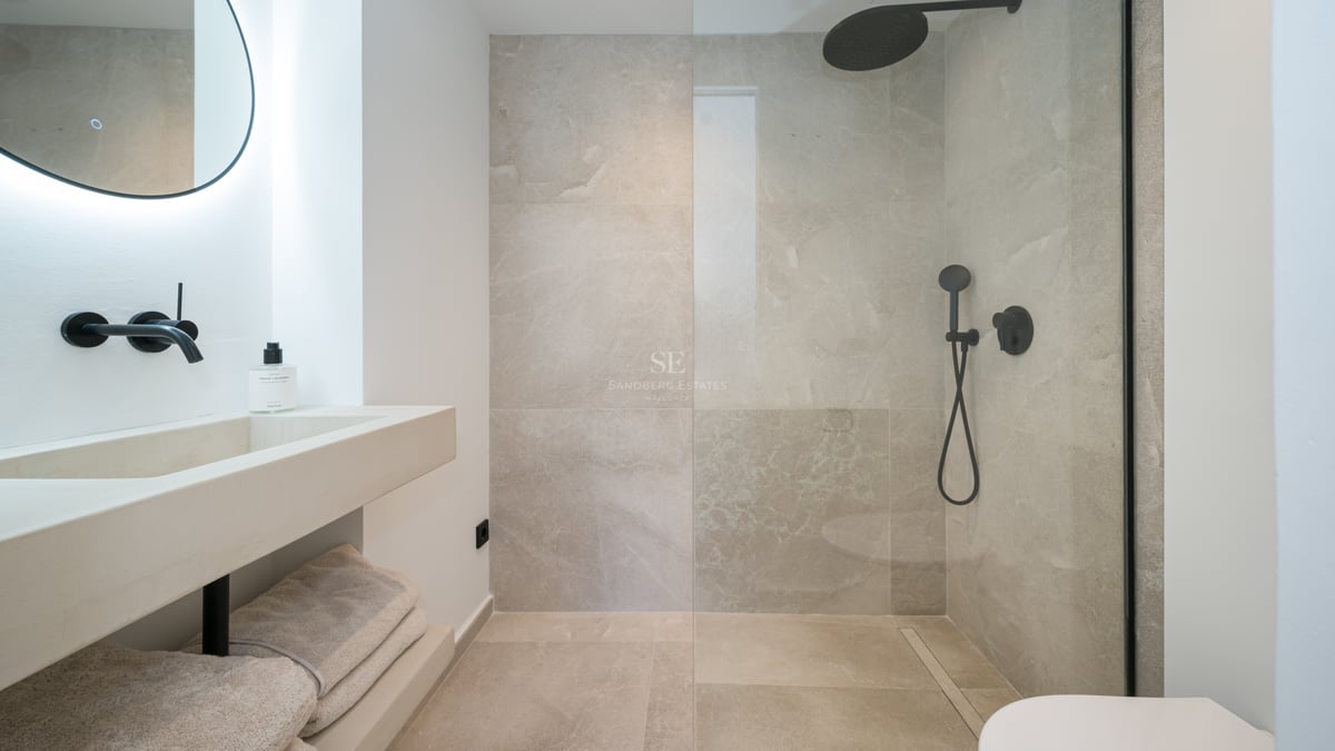 Salle de bain contemporaine avec douche vitrée, carrelage effet pierre et robinetterie noire mate.