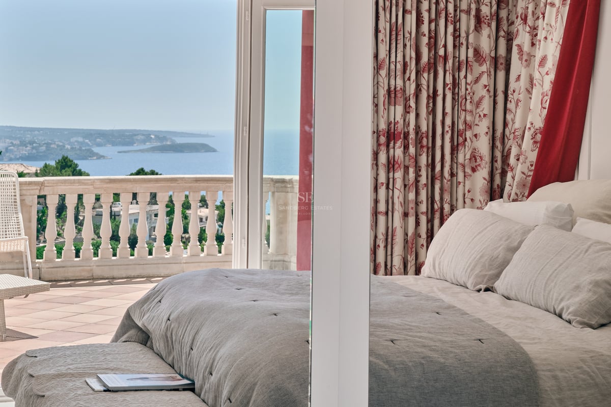 Chambre principale avec linge de lit neutre et terrasse en pierre offrant une vue panoramique sur la mer.