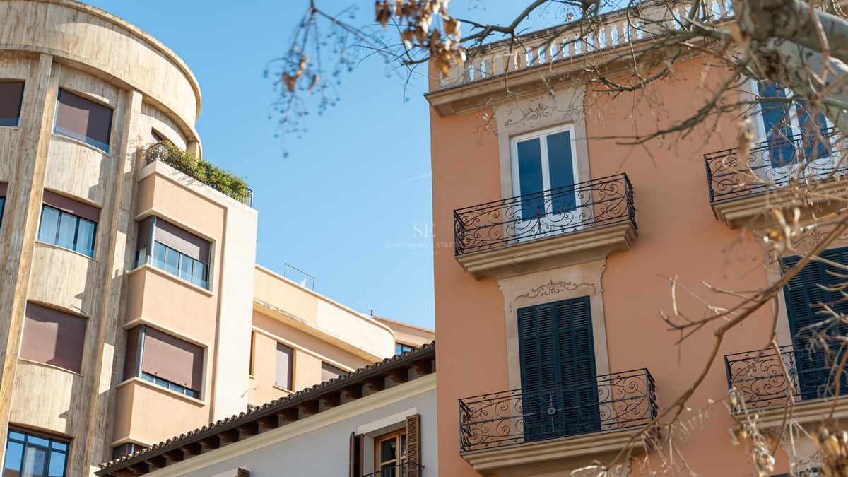 View of historic terracotta and stone building facades with wrought iron balconies against a clear blue sky.
