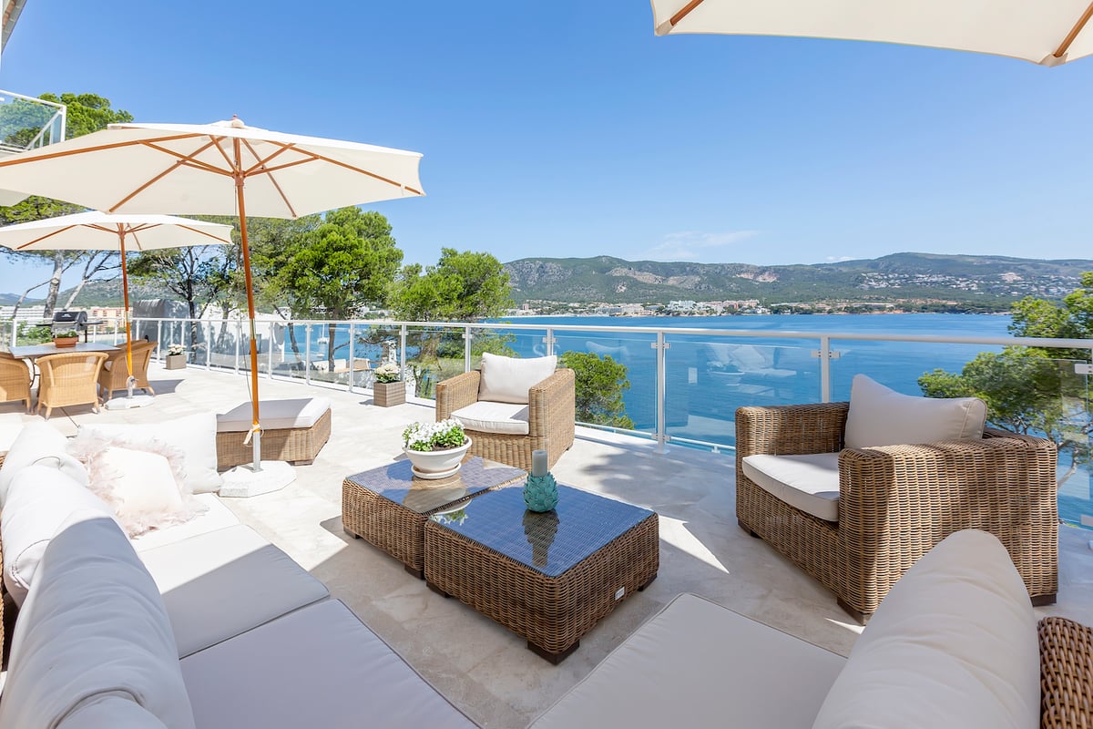 Terrasse ensoleillée avec mobilier en osier, parasols blancs et balustrade en verre surplombant la mer.