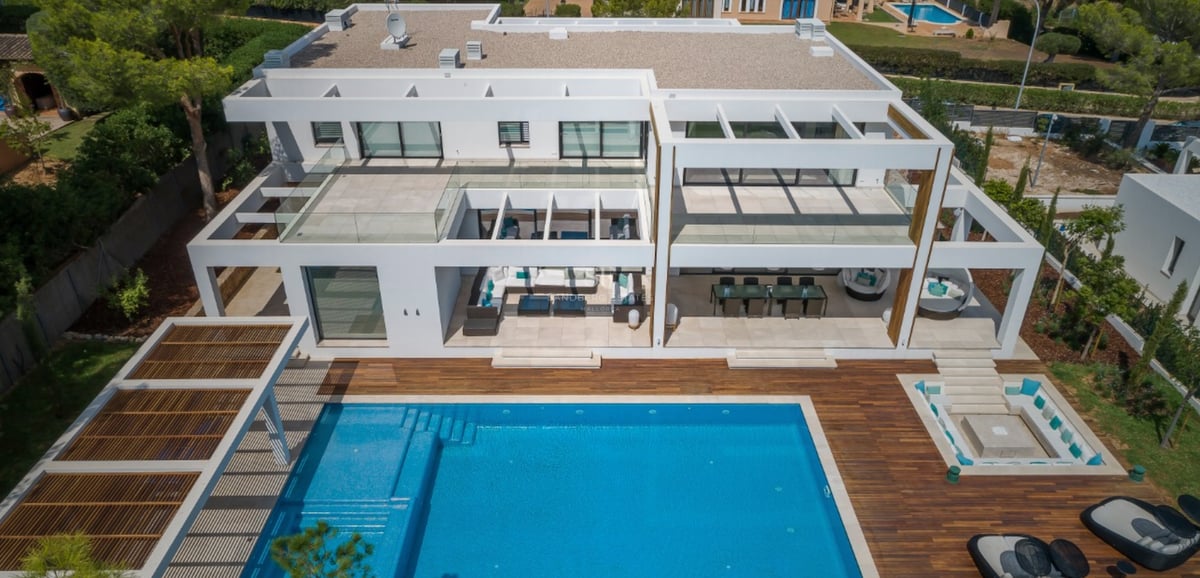 Vue aérienne d'une villa blanche contemporaine avec une grande piscine bleue, terrasse en bois et mobilier d'extérieur.