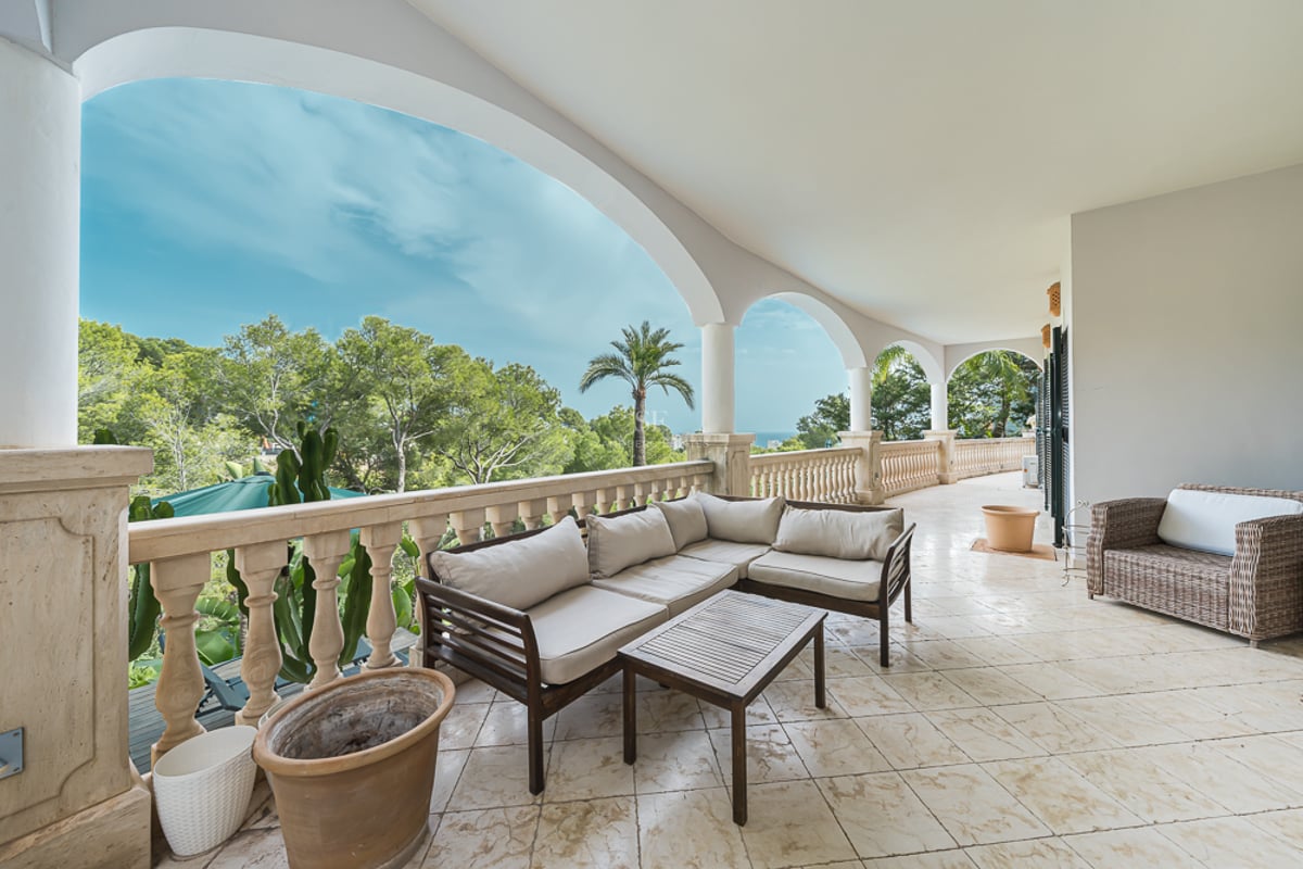 Vaste terrasse voûtée avec salon de jardin, balustrades en pierre et vue sur la végétation luxuriante et la mer.