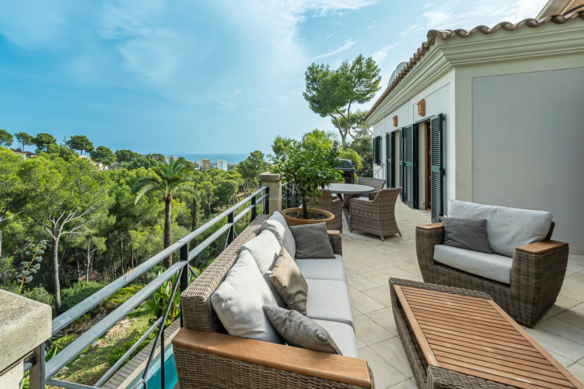 Grande terrasse avec mobilier de salon en rotin et sol en pierre surplombant une vallée verdoyante et la mer.