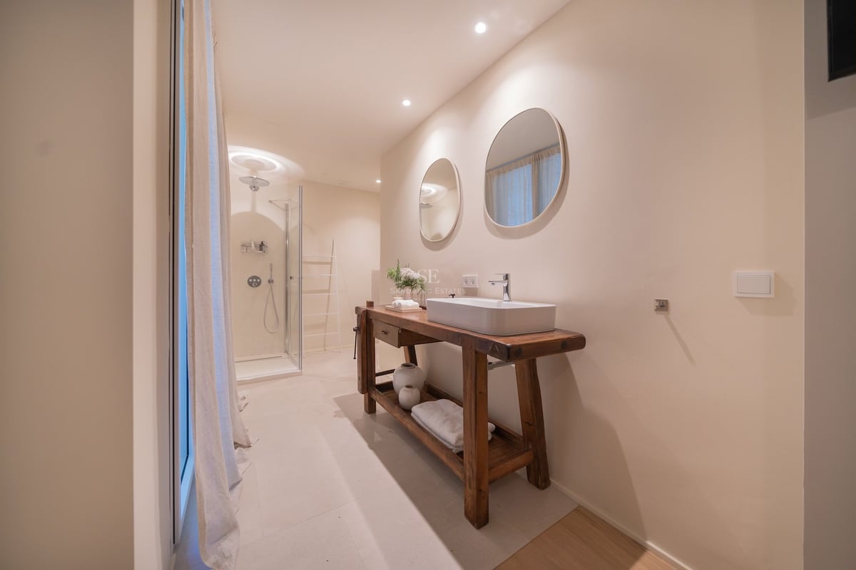 Salle de bains moderne avec meuble en bois massif, vasque à poser, miroirs ronds et douche vitrée.