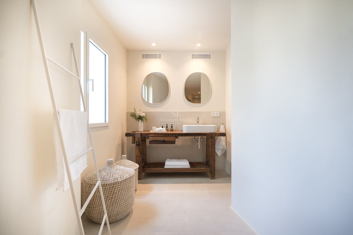 Salle de bains moderne avec meuble en bois de récupération, vasque à poser, miroirs organiques et paniers en osier.