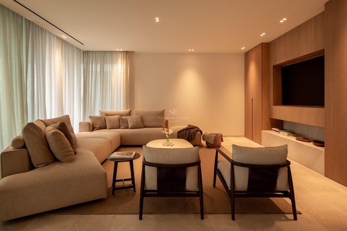Salon élégant avec canapé modulaire beige, boiseries avec TV intégrée et éclairage chaleureux.