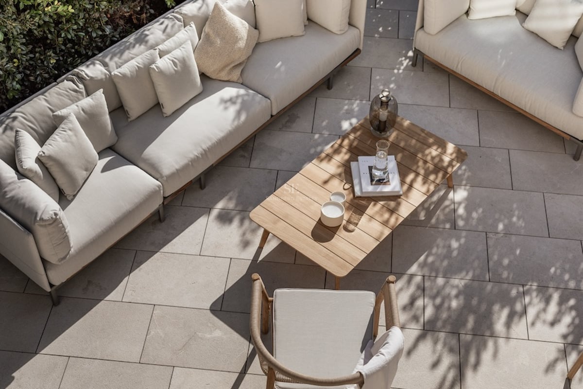 Vue en plongée d'une terrasse de luxe avec canapés beige, table en bois et dallage en pierre sous une lumière tamisée.