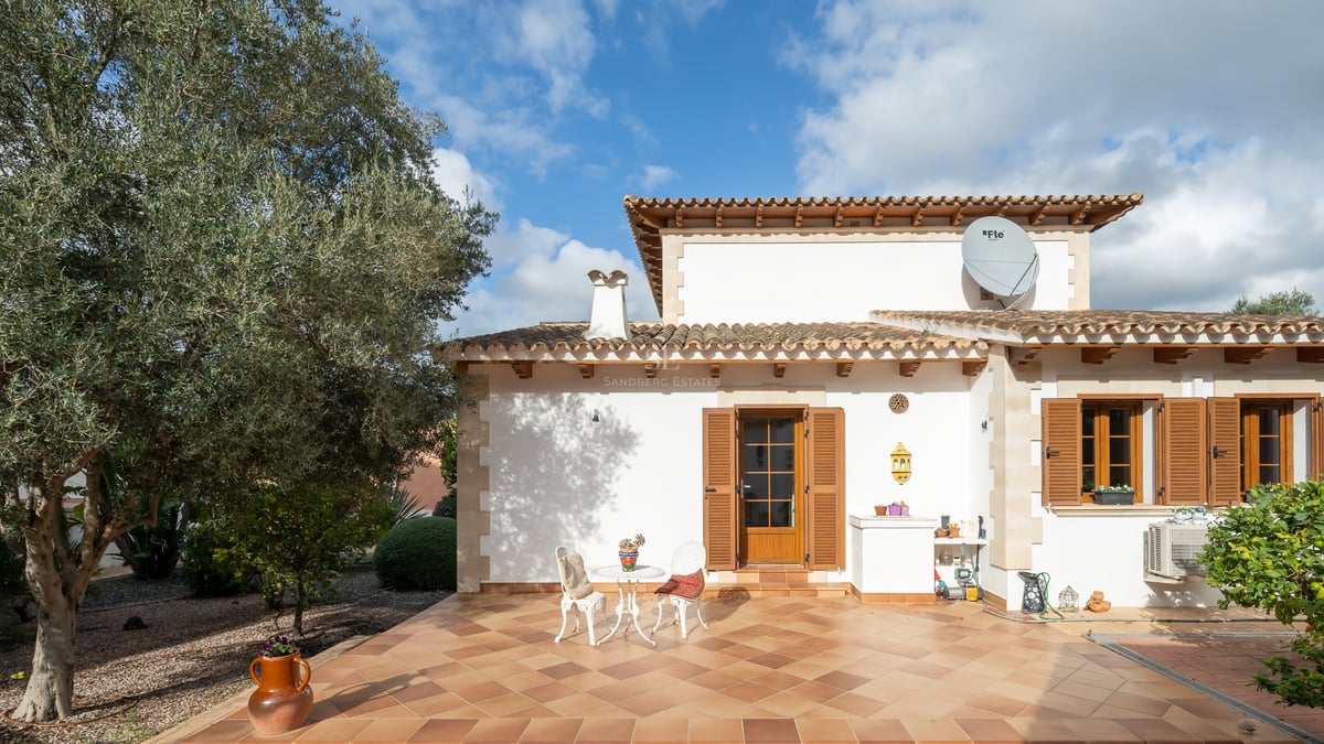 Terrasse de villa avec carrelage en terre cuite, volets en bois, mobilier de jardin blanc et un olivier.