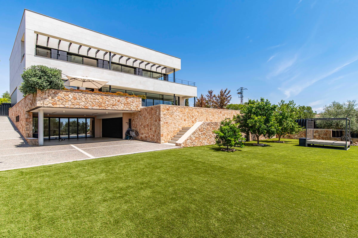 Villa moderne blanche avec murs en pierre naturelle, grande pelouse et aménagement paysager minimaliste.
