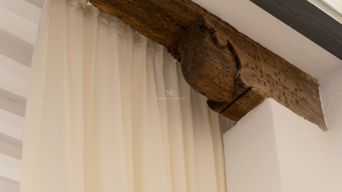 Gros plan d'un corbeau en bois sculpté à la main et d'une poutre sombre à côté de rideaux blancs fluides.