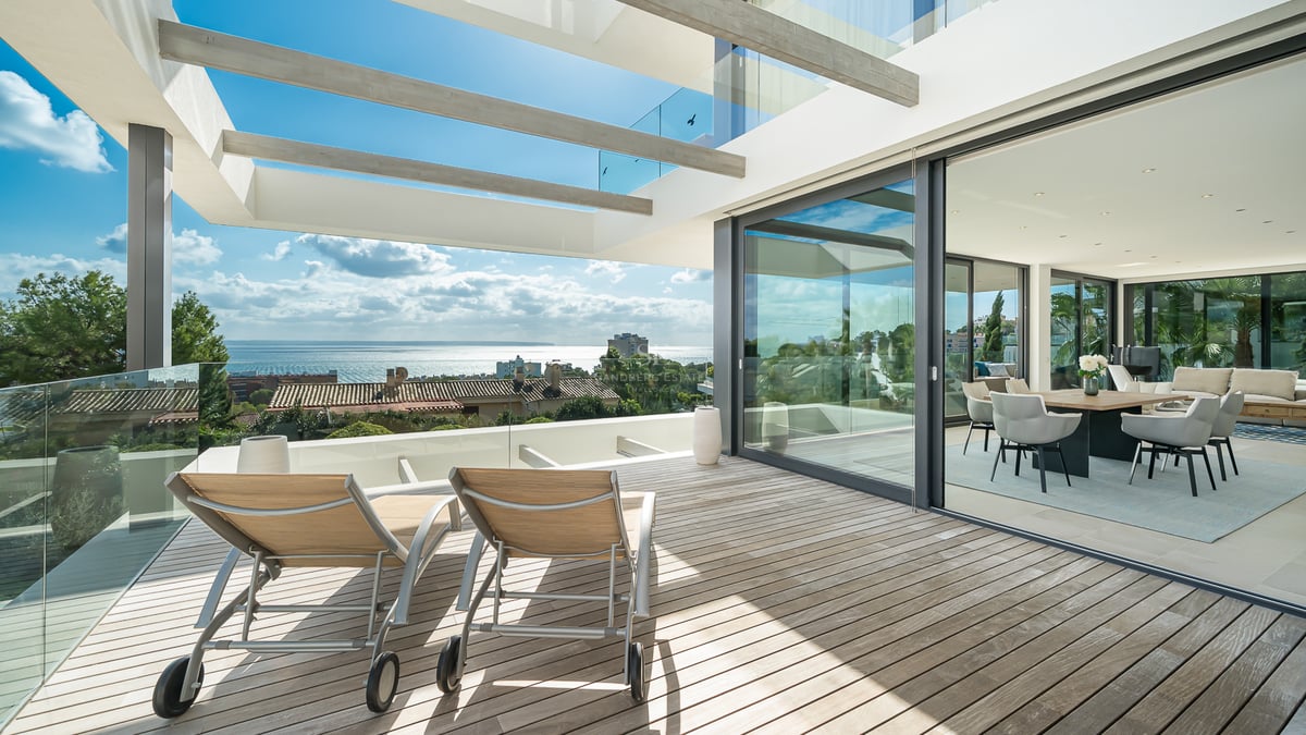 Chaises longues sur une terrasse en bois avec garde-corps en verre surplombant la mer, à côté d'une salle à manger ouverte.